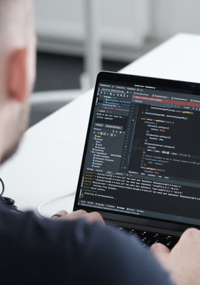 Blick über die Schulter eines Entwicklers auf seinen Laptop Monitor mit Code-Zeilen
