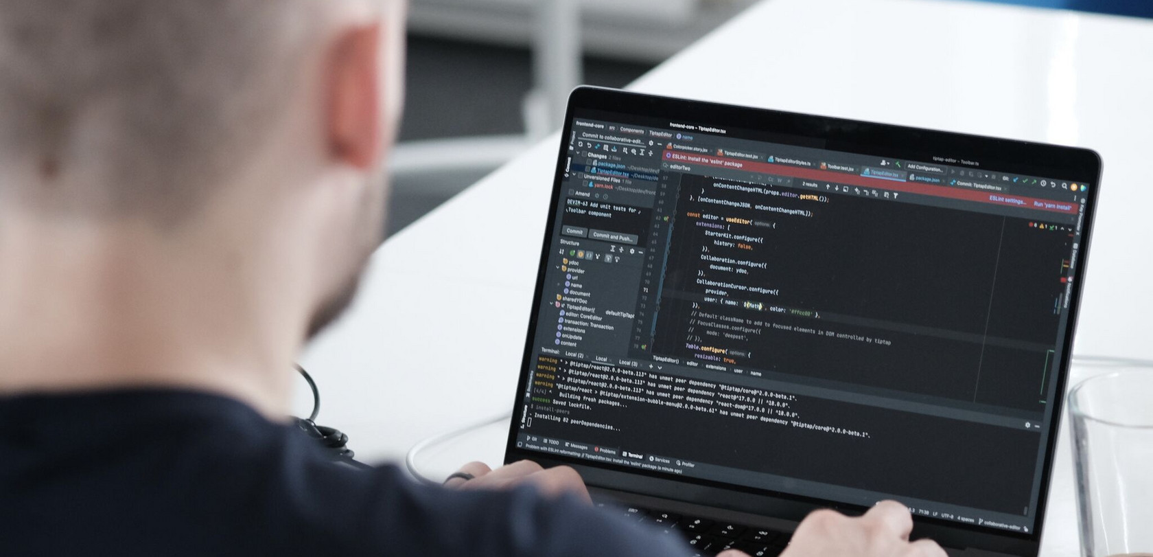 Blick über die Schulter eines Entwicklers auf seinen Laptop Monitor mit Code-Zeilen